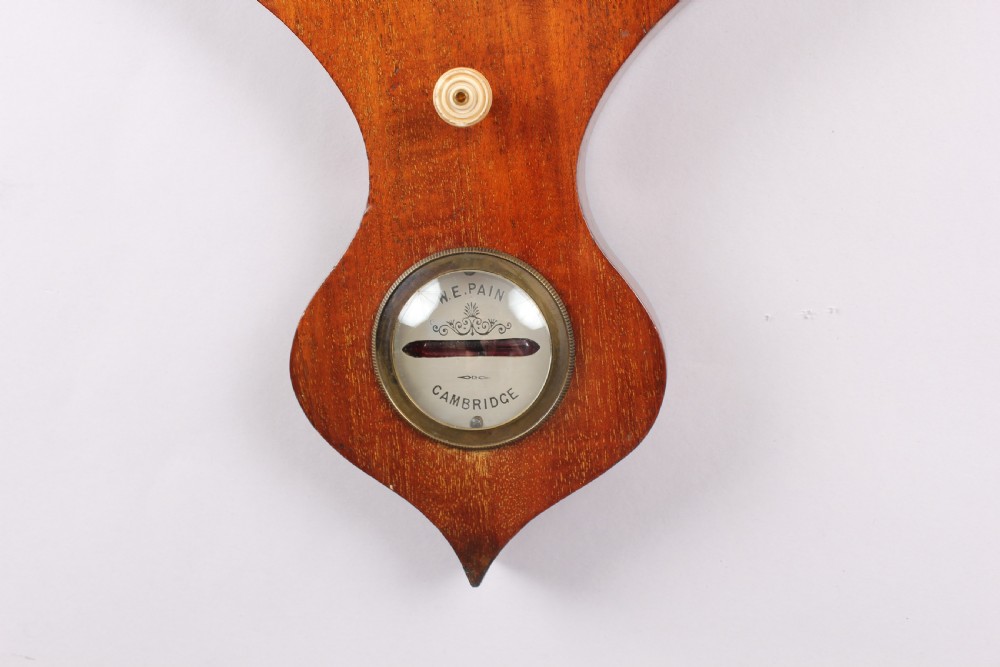 A Victorian mahogany wheel barometer featuring an onion top, upper hygrometer dial, enclosed glass thermometer, central convex mirror, silvered main dial, and lower spirit level plate by W.E. Pain of Cambridge. View IV