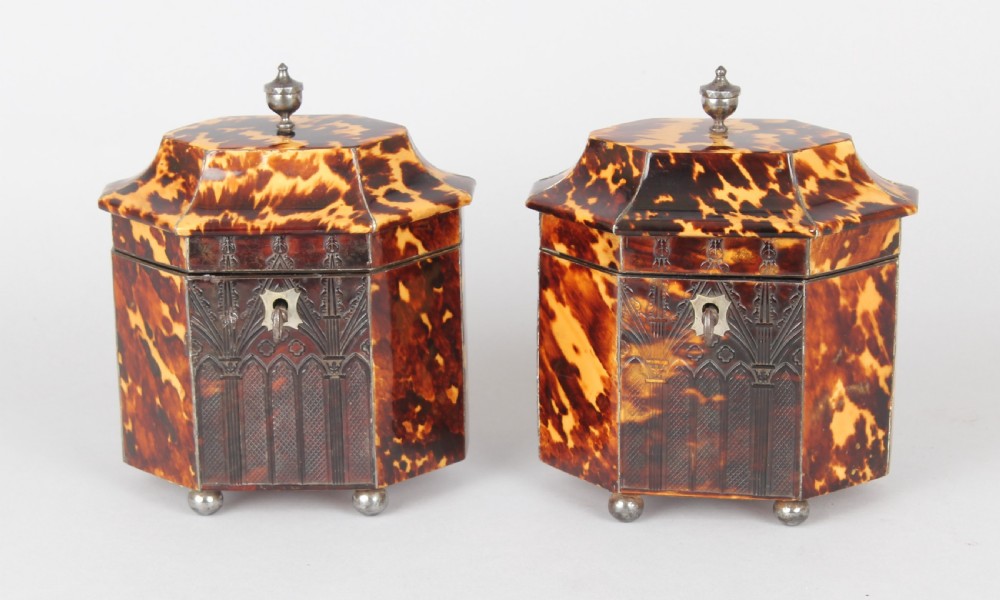 A pair of octagonal George IV period miniature tea caddies crafted with mottled tortoiseshell veneer, silver urn finials, ball feet, and gothic arcading.