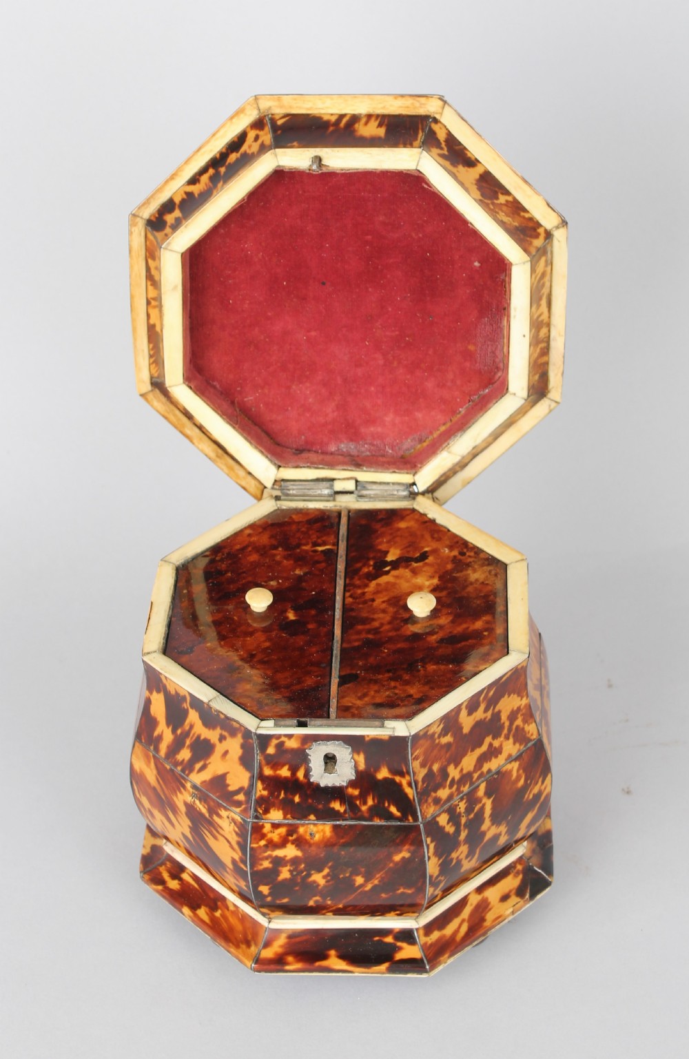 An octagonal Regency period tea caddy decorated with mottled amber tortoiseshell veneer, a carved rosette finial, and a silver escutcheon. View V