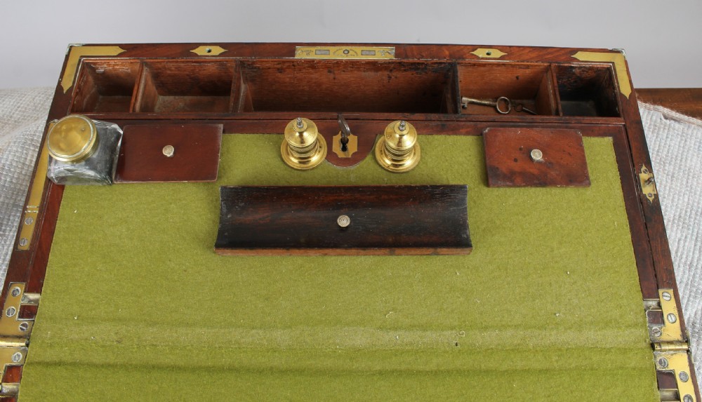 An open antique mahogany writing box with brass corner mounts, revealing a green baize writing surface, internal pen tray compartments, and a stationers paper label inside the lid. View II