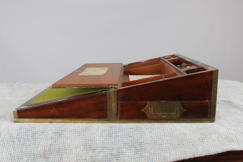 An open antique mahogany writing box with brass corner mounts, revealing a green baize writing surface, internal pen tray compartments, and a stationers paper label inside the lid. View III