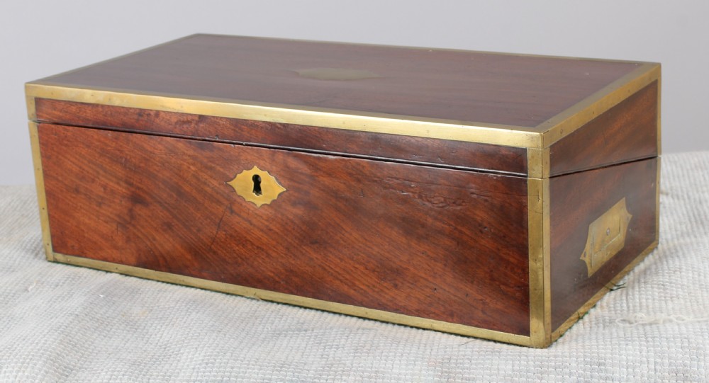An open antique mahogany writing box with brass corner mounts, revealing a green baize writing surface, internal pen tray compartments, and a stationers paper label inside the lid. View V