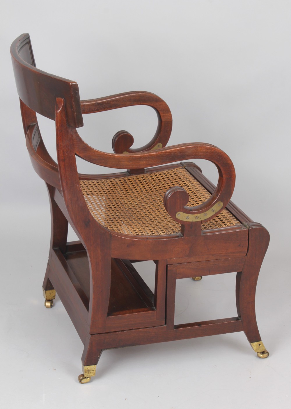 A Regency period mahogany metamorphic library chair with scroll armrests, a buttoned leather seat, and brass castors. View IV