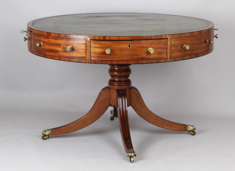 A Regency mahogany drum table featuring a green leather inset top, frieze drawers with brass handles, and a turned pedestal with four splayed reeded legs on brass castors.