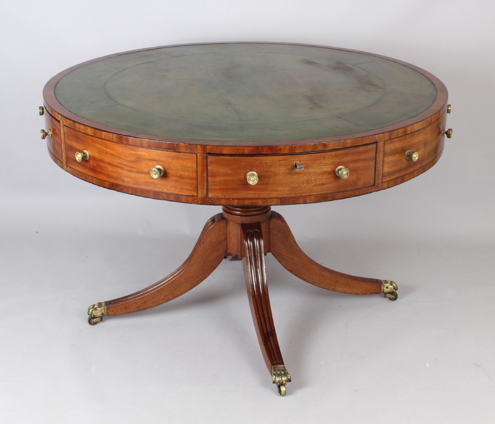 A Regency mahogany drum table featuring a green leather inset top, frieze drawers with brass handles, and a turned pedestal with four splayed reeded legs on brass castors. View II