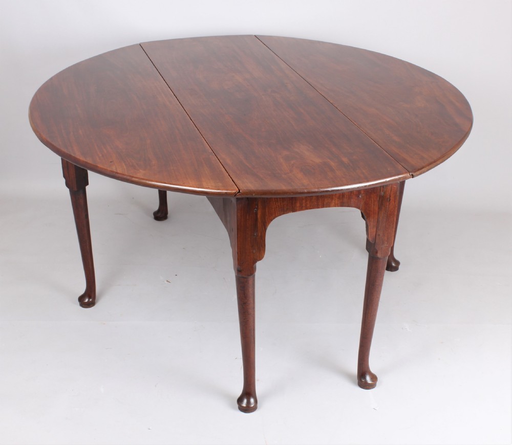 An 18th-century oval mahogany drop-leaf dining table supported by slender cabriole legs ending in pad feet.
