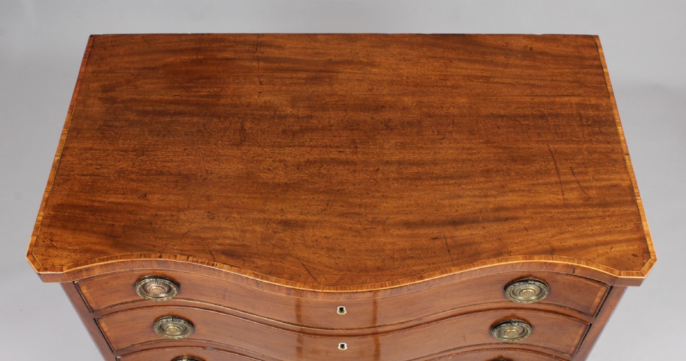 A late eighteenth-century mahogany serpentine chest of drawers featuring four graduated drawers with brass handles resting on bracket feet. View III