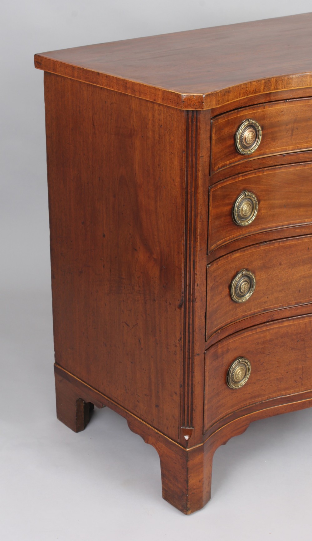 A late eighteenth-century mahogany serpentine chest of drawers featuring four graduated drawers with brass handles resting on bracket feet. View IV