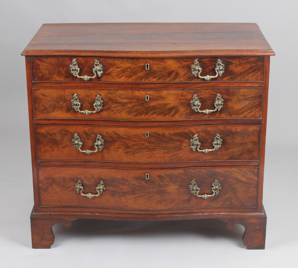 A Georgian style warm brown mahogany serpentine chest of drawers featuring four graduated drawers with rococo brass handles and bracket feet. View II