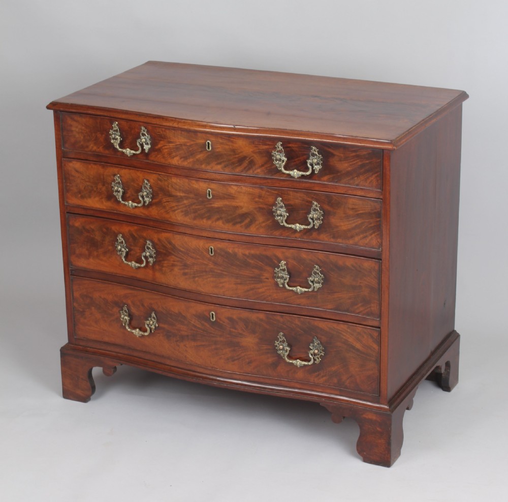 A Georgian style warm brown mahogany serpentine chest of drawers featuring four graduated drawers with rococo brass handles and bracket feet. View III
