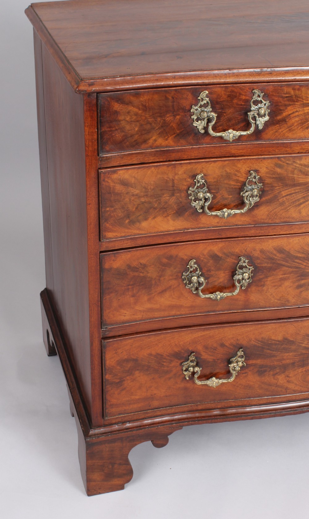 A Georgian style warm brown mahogany serpentine chest of drawers featuring four graduated drawers with rococo brass handles and bracket feet. View IV