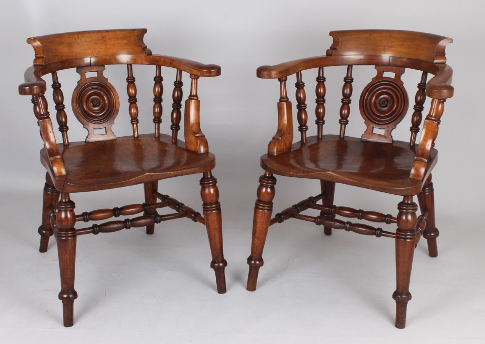A pair of 19th-century satin birch smokers bow armchairs featuring turned spindles, central carved roundel splats, and shaped wooden seats.