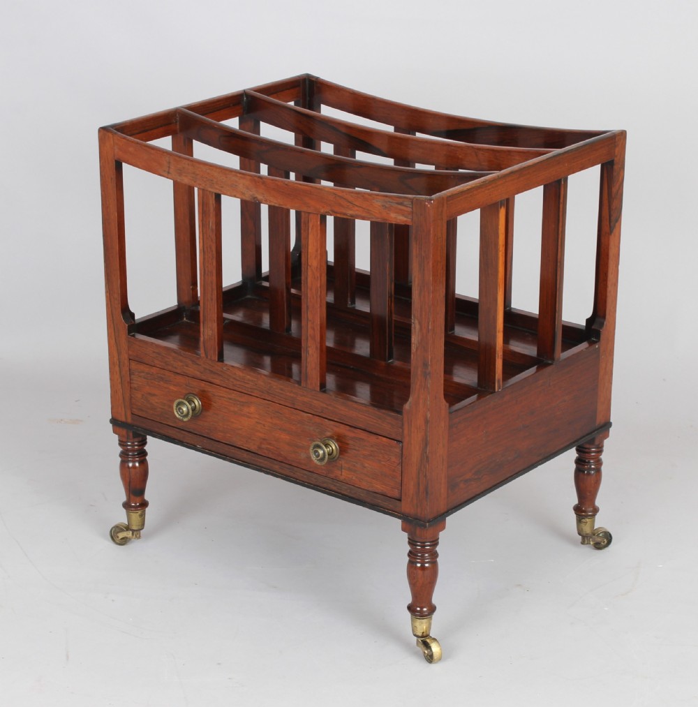 An antique George IV rosewood canterbury featuring three upper divisions, slatted side panels, a lower drawer with brass knobs, and turned legs with brass castors.