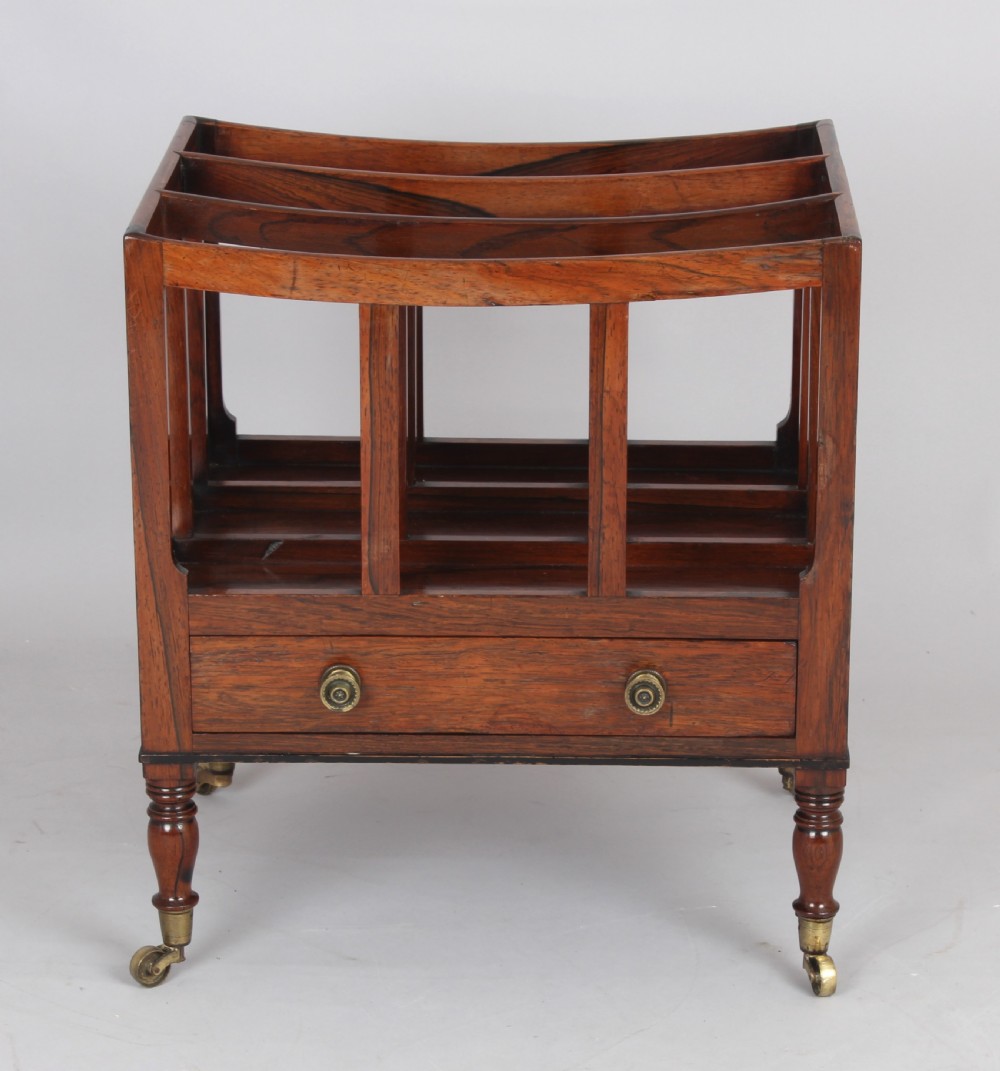 An antique George IV rosewood canterbury featuring three upper divisions, slatted side panels, a lower drawer with brass knobs, and turned legs with brass castors. View II