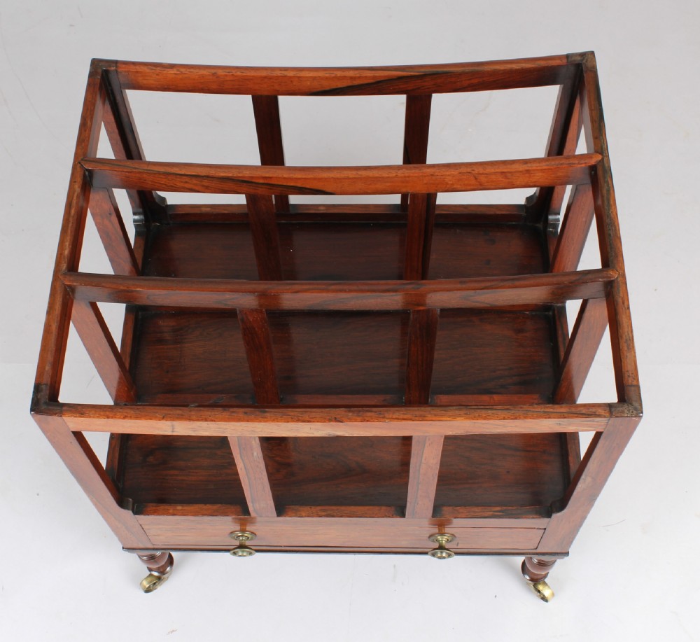 An antique George IV rosewood canterbury featuring three upper divisions, slatted side panels, a lower drawer with brass knobs, and turned legs with brass castors. View III