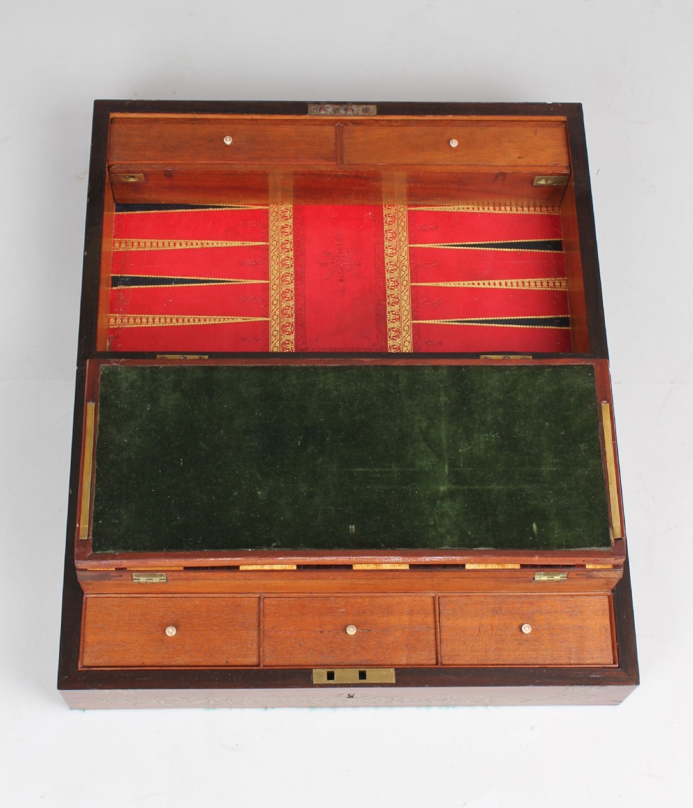 An open early Victorian rosewood games compendium featuring small wooden drawers, a green velvet playing surface, and a red gilt-tooled backgammon interior section.