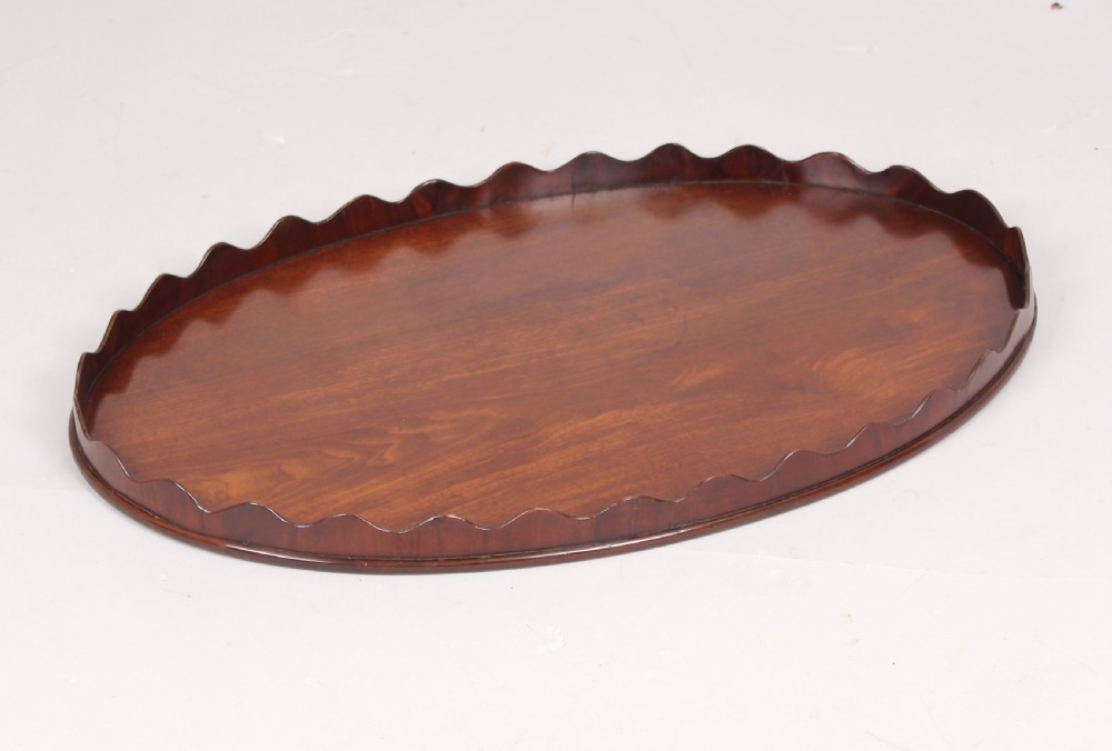 A polished George III period oval mahogany tray featuring a raised scalloped rim and warm wood grain.