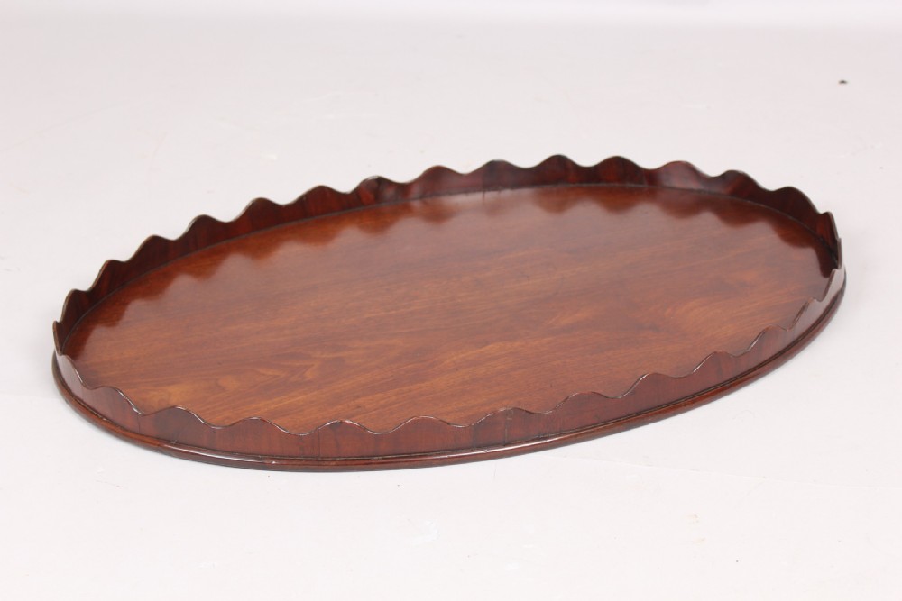 A polished George III period oval mahogany tray featuring a raised scalloped rim and warm wood grain. View II