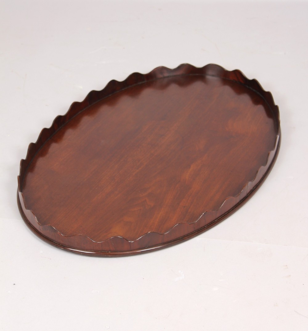 A polished George III period oval mahogany tray featuring a raised scalloped rim and warm wood grain. View III