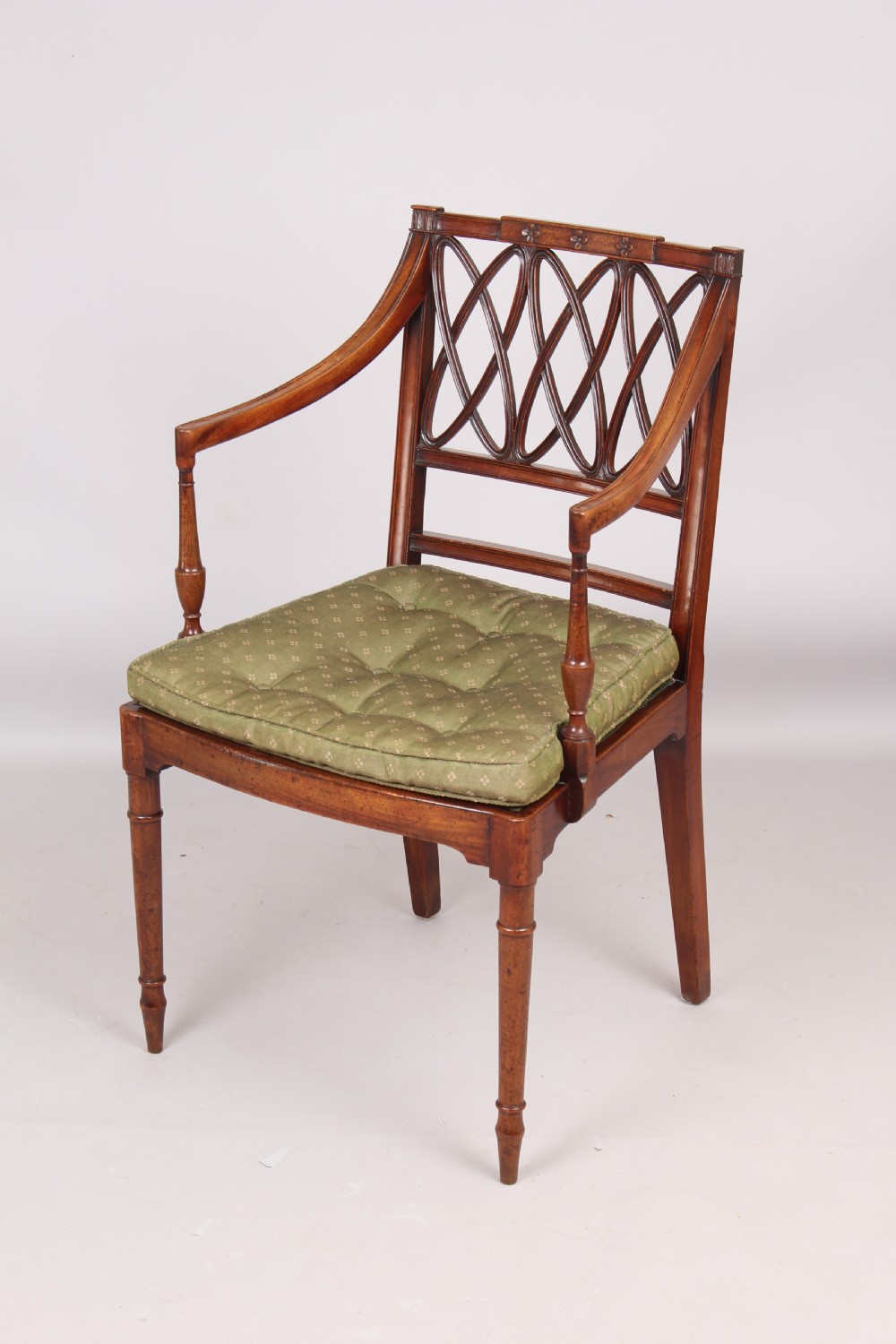 A pair of antique George III mahogany elbow chairs featuring openwork lattice backs, swept armrests, turned front legs, and green seat cushions. View II