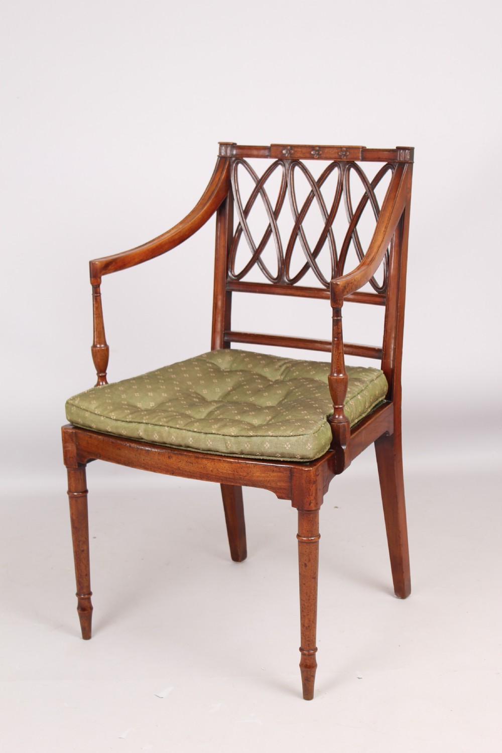 A pair of antique George III mahogany elbow chairs featuring openwork lattice backs, swept armrests, turned front legs, and green seat cushions. View III