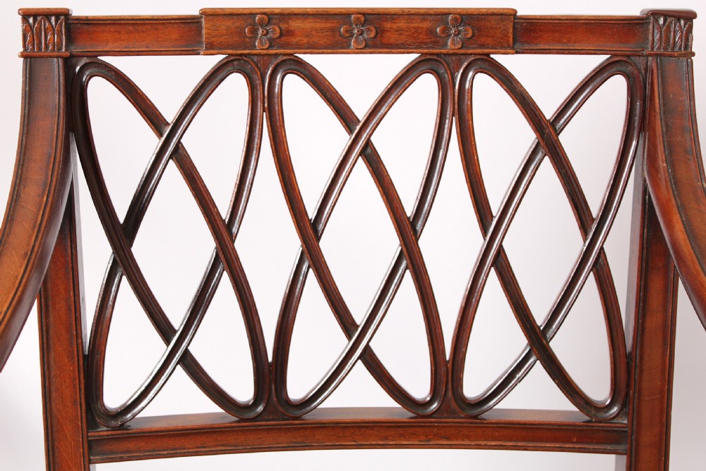 A pair of antique George III mahogany elbow chairs featuring openwork lattice backs, swept armrests, turned front legs, and green seat cushions. View V