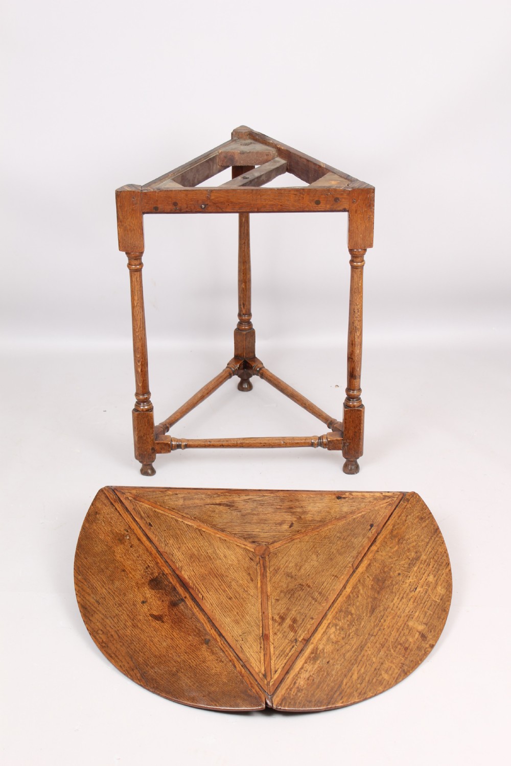 An early 18th-century oak cricket table featuring a triangular top with drop leaves, turned legs, and a triangular stretcher base. View V