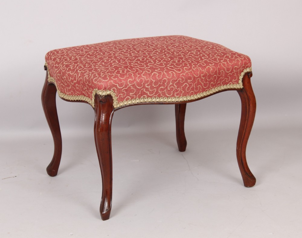 A Victorian mahogany stool featuring four carved cabriole legs and a patterned red upholstered rectangular seat trimmed with braid.
