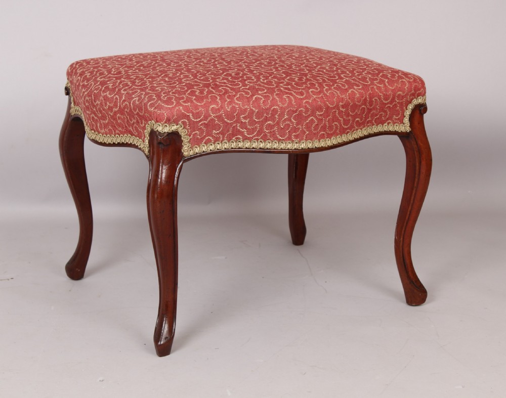 A Victorian mahogany stool featuring four carved cabriole legs and a patterned red upholstered rectangular seat trimmed with braid. View II