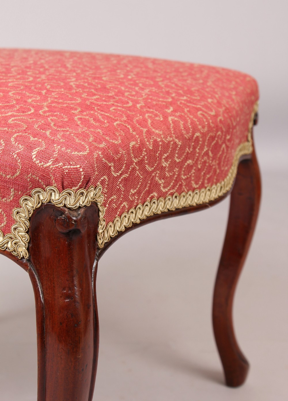 A Victorian mahogany stool featuring four carved cabriole legs and a patterned red upholstered rectangular seat trimmed with braid. View III