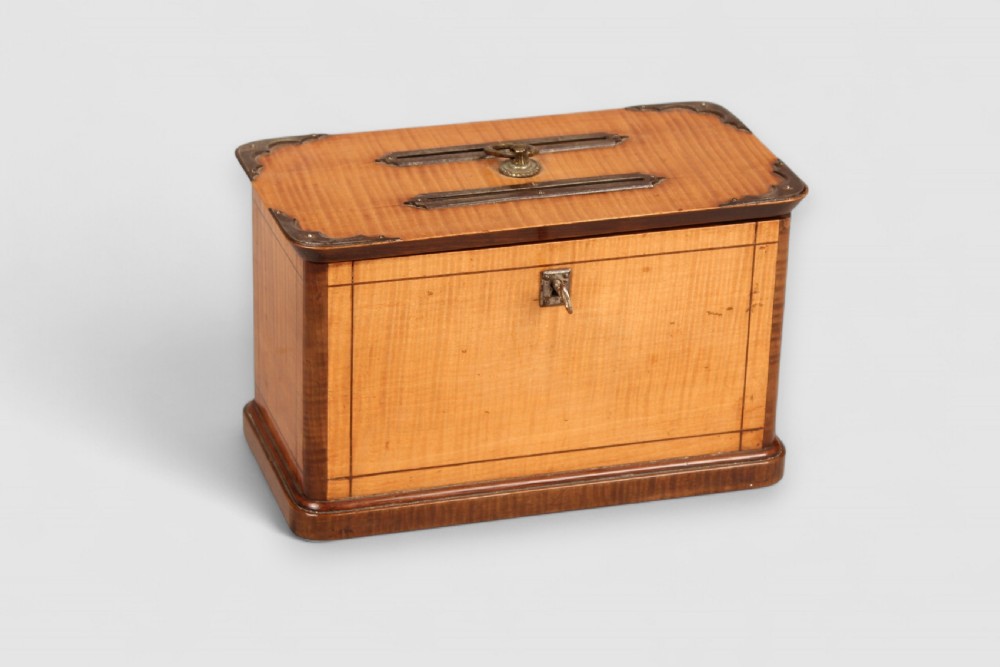 A nineteenth-century rectangular wooden ballot box featuring satinwood veneer with dark wood borders, brass corner mounts, twin top slots with a central ring handle, and a front keyhole.