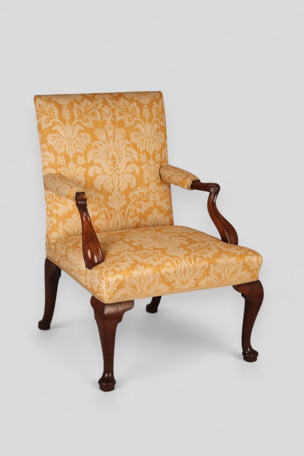 A mid-18th-century Georgian open armchair crafted from dark mahogany, featuring cabriole front legs, swept rear legs, and gold-yellow damask upholstery.
