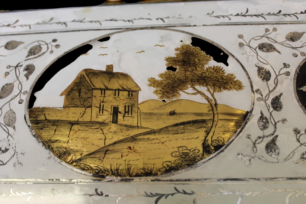 A vertical Regency giltwood wall mirror with fluted side columns, a breakfront cornice with spherules, and a reverse-painted glass panel depicting a cottage landscape above the main glass plate. View III