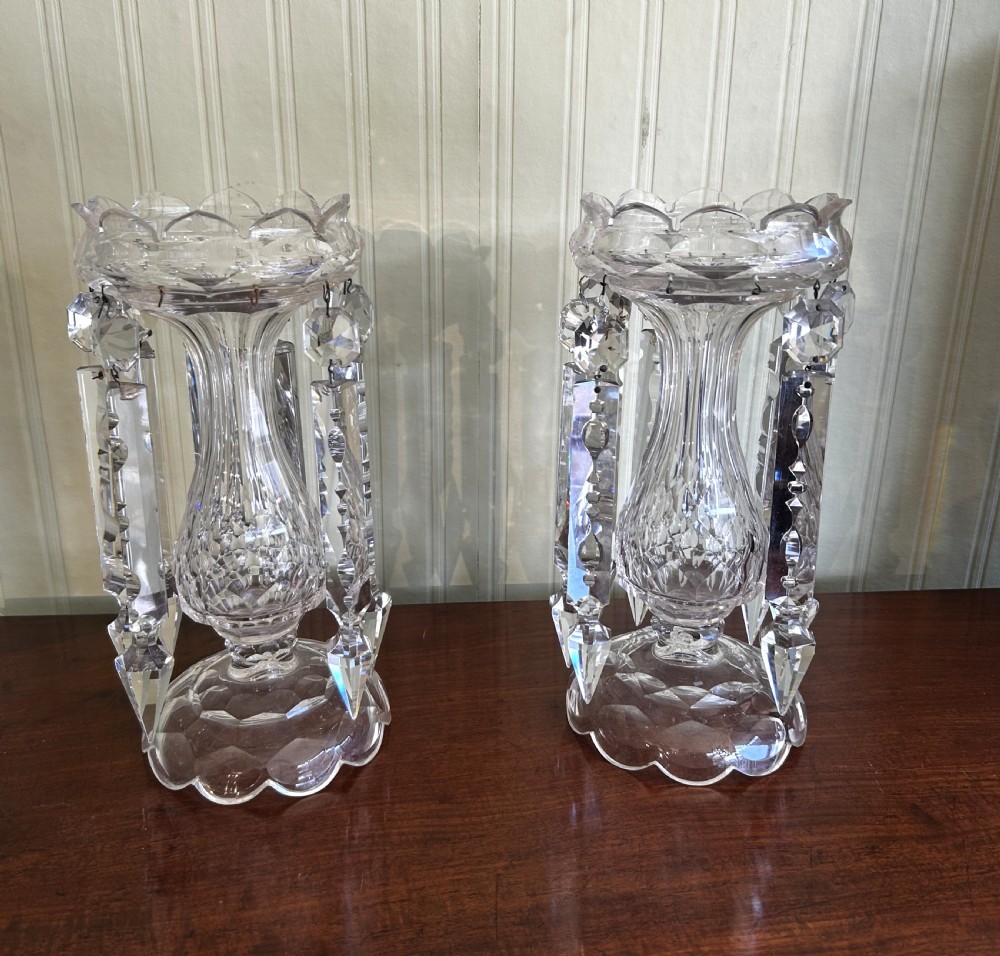A pair of clear Victorian cut-glass lustres featuring faceted baluster stems, scalloped top rims, and hanging crystal prism drops.