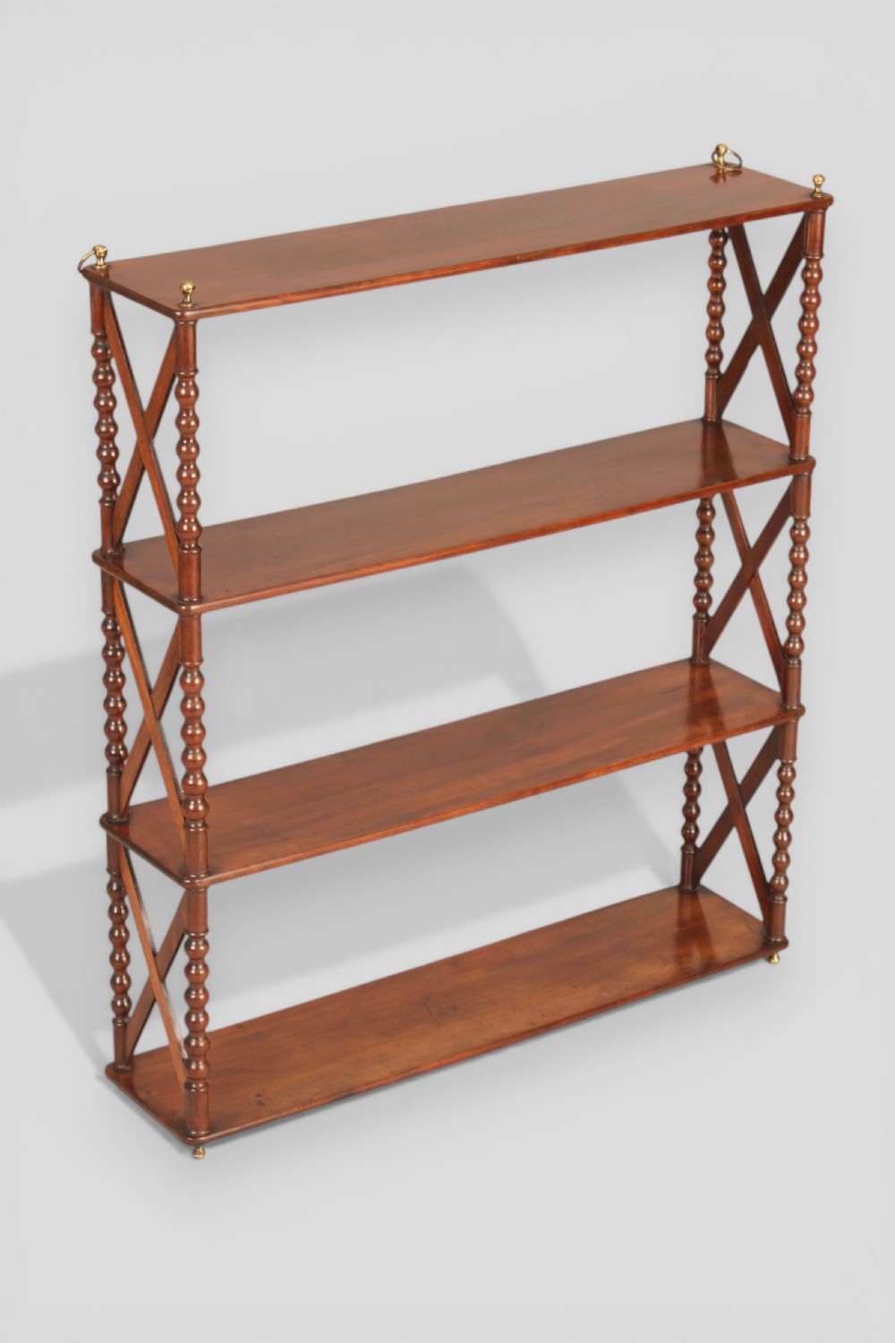 A four-tier dark mahogany hanging shelf unit featuring bobbin-turned vertical posts, X-frame lattice sides, and top brass hanging fixtures.