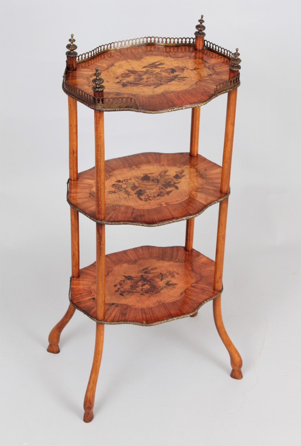 A three-tiered mid 19th century French-style wooden etagere featuring floral marquetry inlays, turned upright supports, brass finials, and a pierced brass gallery on the top shelf.