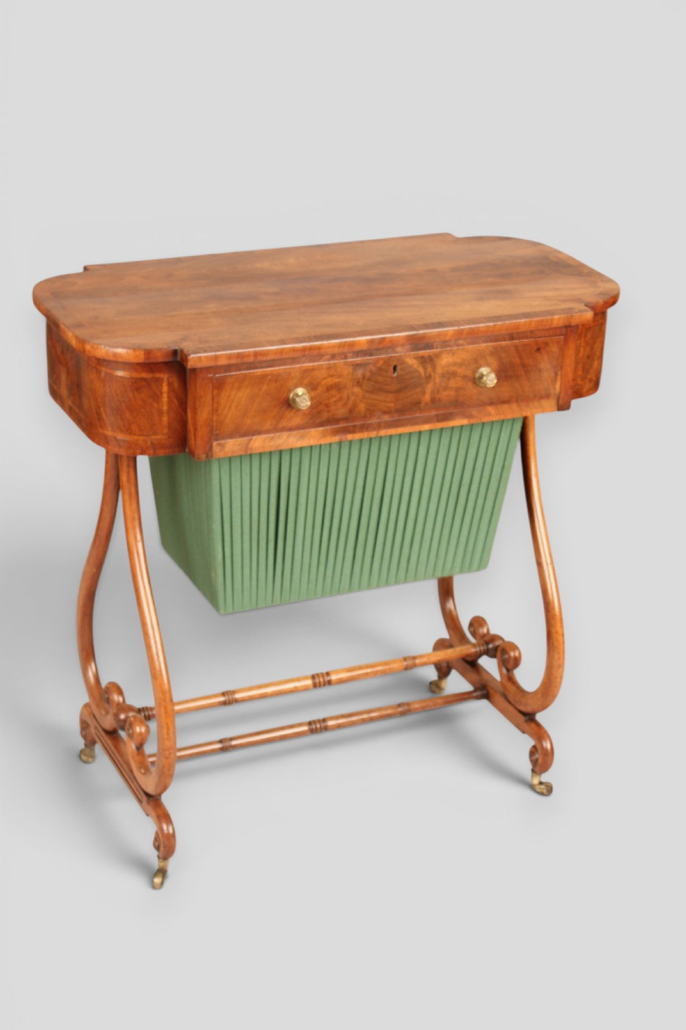 A Regency mahogany work table featuring a single drawer above a pleated green fabric basket, supported by lyre-shaped ends and a double stretcher with castors. View III