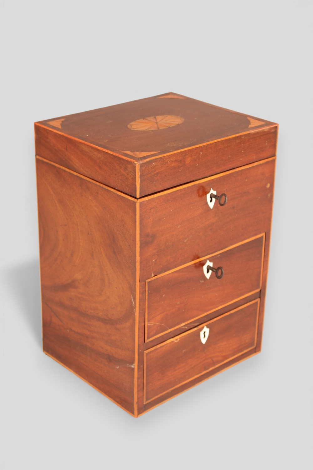 A George III mahogany apothecary box featuring marquetry inlay on the hinged lid and three stacked drawers with shield-shaped bone escutcheons.
