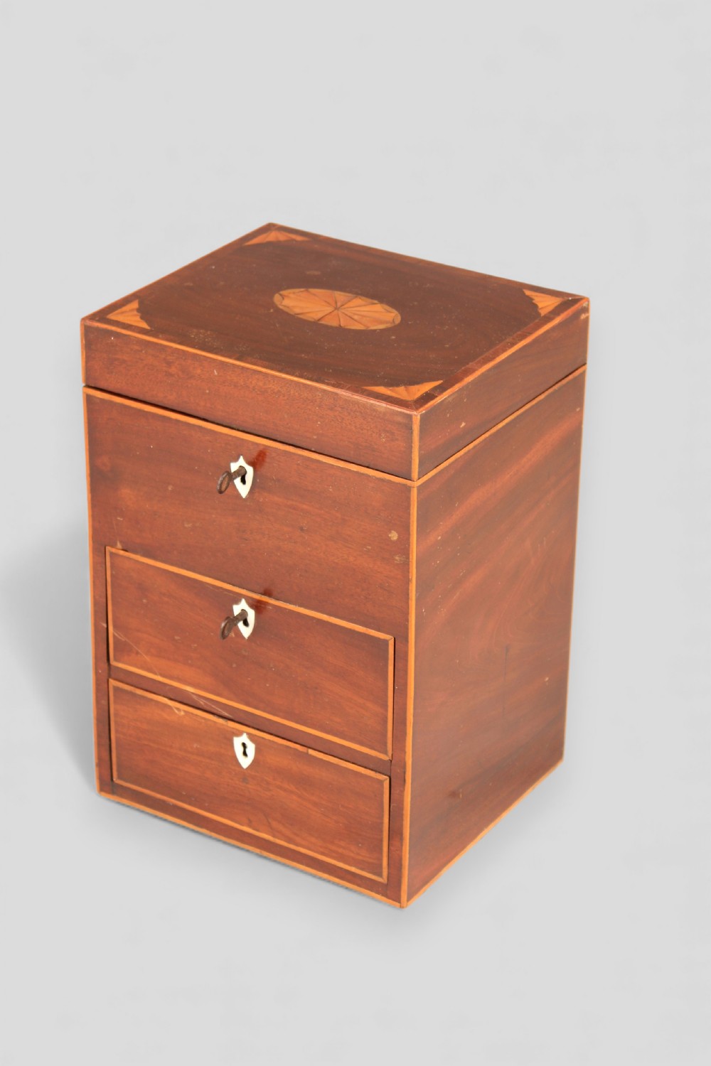 A George III mahogany apothecary box featuring marquetry inlay on the hinged lid and three stacked drawers with shield-shaped bone escutcheons. View II