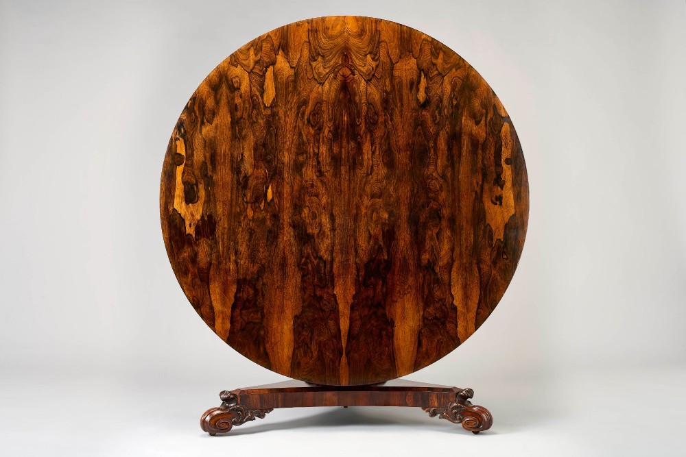 A large George IV circular tilt-top dining or centre table in highly figured book-matched rosewood veneer on a carved triform base.