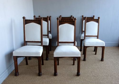 fig 2. Set of six Gothic Revival oak dining chairs featuring pointed arch upholstered backs, carved cresting, turned finials, and white fabric upholstery.