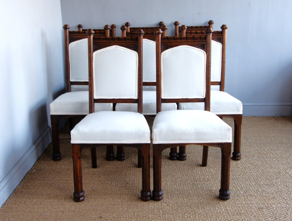 Set of six Gothic Revival oak dining chairs featuring pointed arch upholstered backs, carved cresting, turned finials, and white fabric upholstery. View II