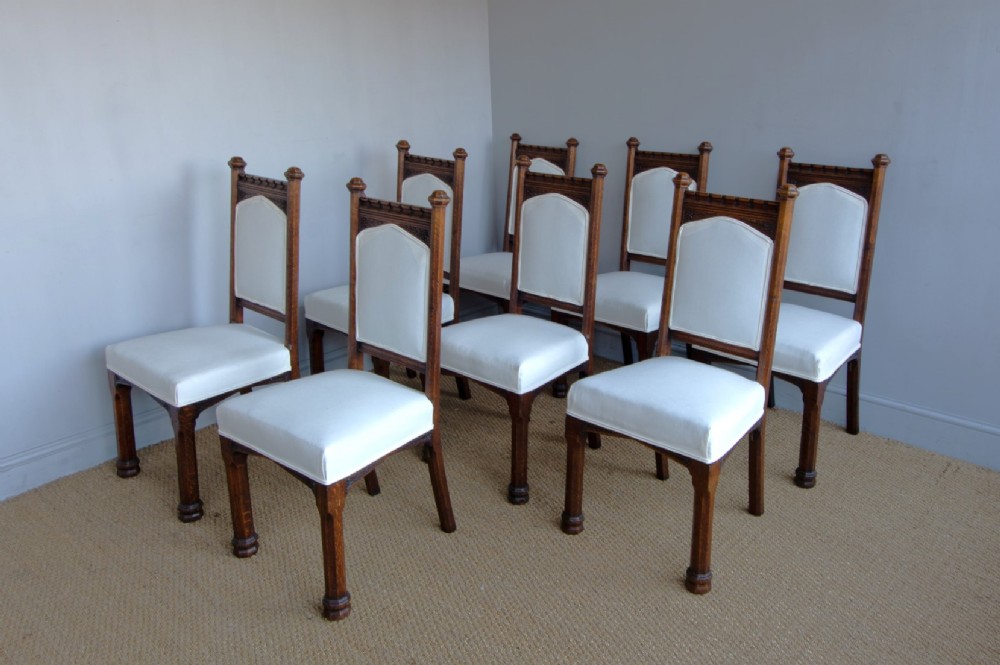 Set of six Gothic Revival oak dining chairs featuring pointed arch upholstered backs, carved cresting, turned finials, and white fabric upholstery. View IV