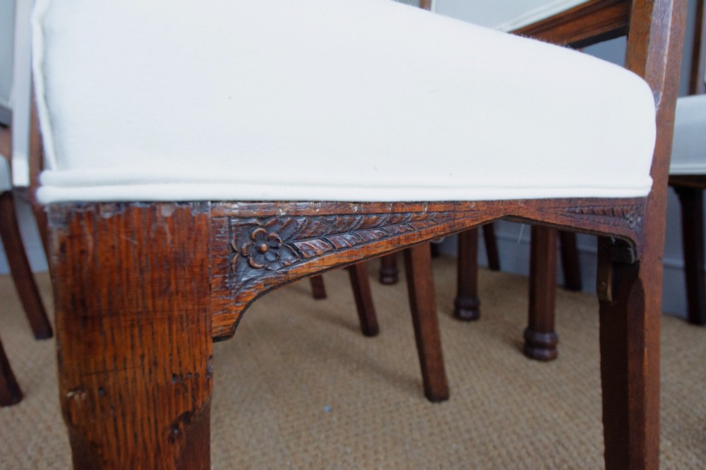 Set of six Gothic Revival oak dining chairs featuring pointed arch upholstered backs, carved cresting, turned finials, and white fabric upholstery. View V