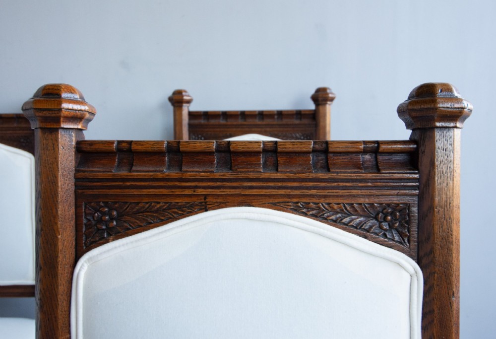 Set of six Gothic Revival oak dining chairs featuring pointed arch upholstered backs, carved cresting, turned finials, and white fabric upholstery. View VI