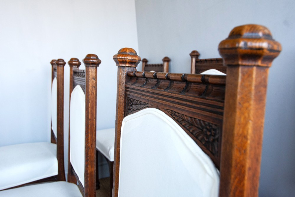 Set of six Gothic Revival oak dining chairs featuring pointed arch upholstered backs, carved cresting, turned finials, and white fabric upholstery. View VII