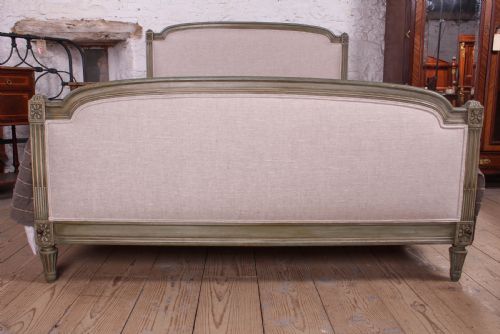 fig 1. A Louis XVI style French king-size bed frame featuring a muted green painted wooden trim, fluted corner posts, rosettes, and cream linen upholstered panels on the headboard and footboard.