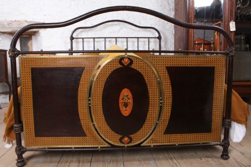 fig 1. An antique European double bed featuring a dark iron frame, brass top rails, vertical spindles on the headboard, and decorative painted panel inserts on the footboard.
