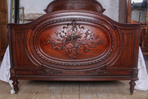 fig 1. A French rosewood bed frame with a high arched headboard and a carved floral oval cartouche on the footboard.