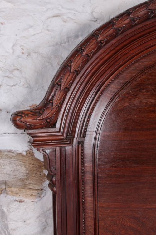 fig 3. A French rosewood bed frame with a high arched headboard and a carved floral oval cartouche on the footboard.